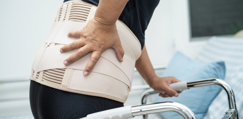 Person wearing a back brace holds their lower back in pain while using a walker for support
