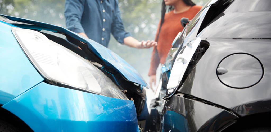 Two damaged cars, one blue and one black, with a man and a woman discussing the accident in the background