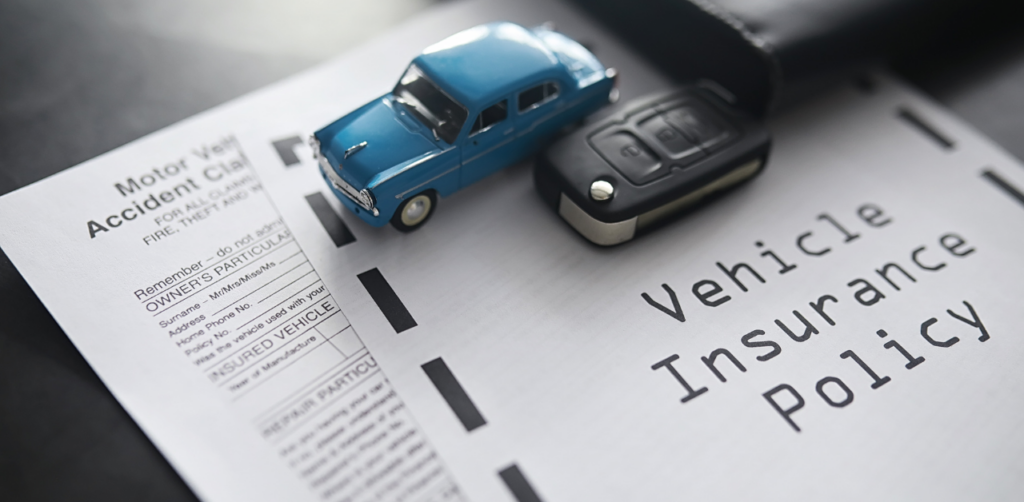 Vehicle insurance policy document with a toy car, car key, and accident claim form placed on top