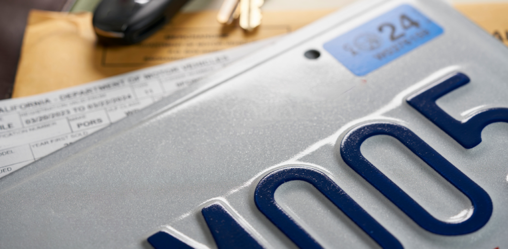 Close-up of a California license plate with a registration sticker and DMV paperwork in the background