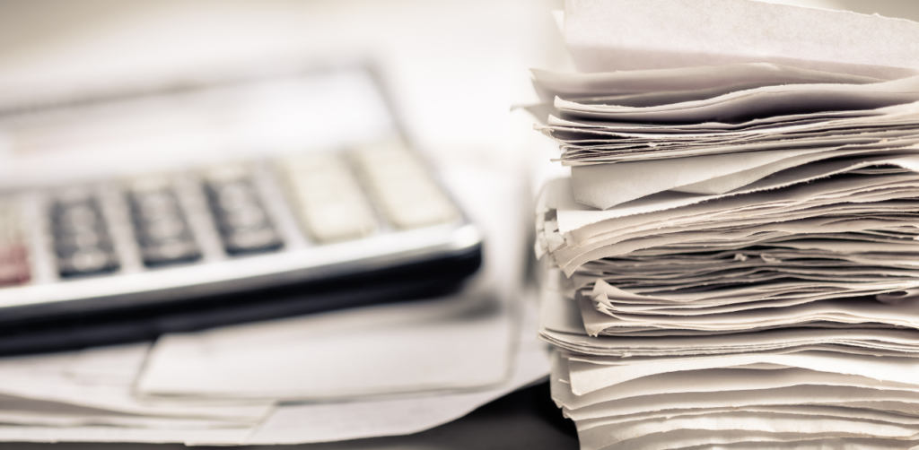 A tall stack of paperwork with a calculator beside it