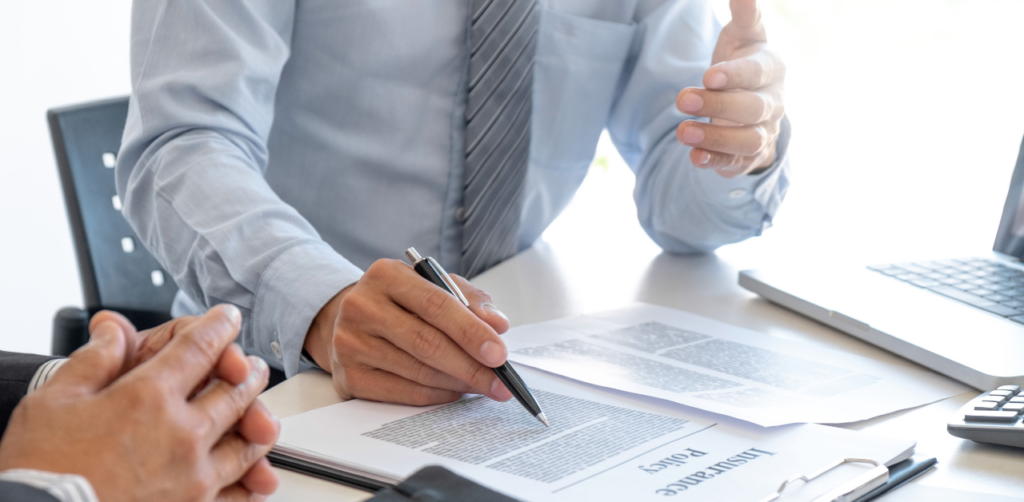 Business professional in a suit discussing an insurance policy with a client, pointing at legal documents on a table