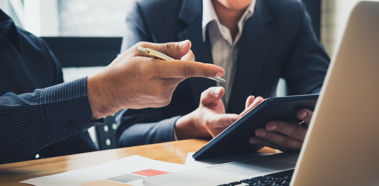 Business professionals in suits discussing data on a tablet and laptop during a meeting