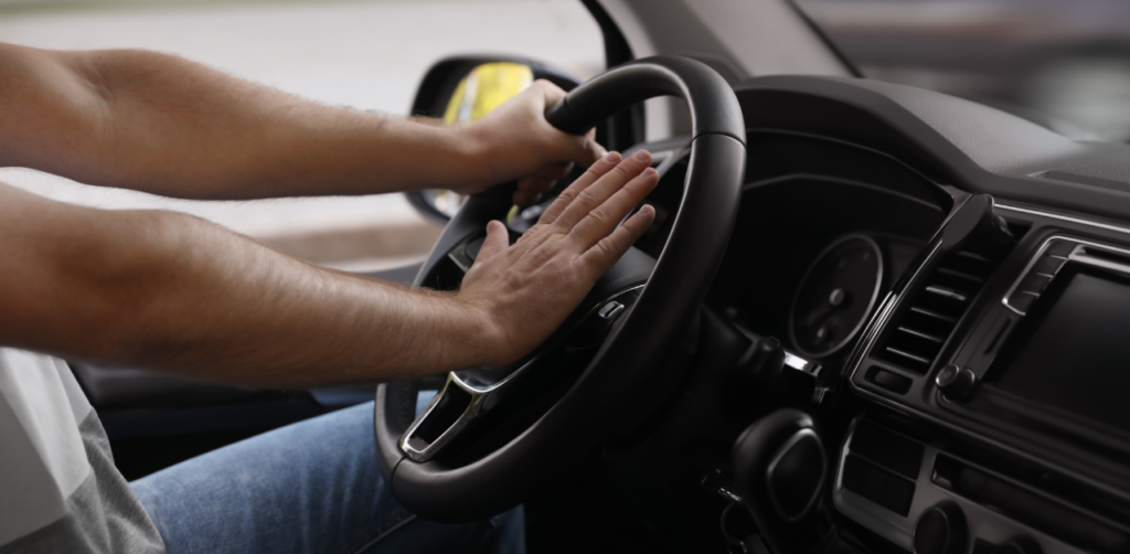 Close-up of a driver's hands pressing the car horn while gripping the steering wheel, indicating urgency or frustration