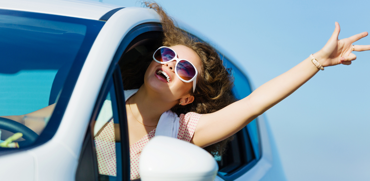 Happy young woman leaning out of a white car window, smiling and enjoying the breeze