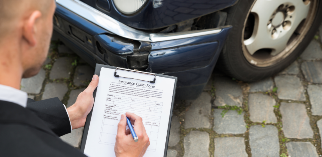 Man filling out an insurance claim form near a damaged car with a dented front bumper