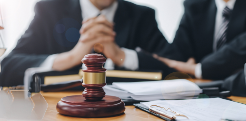 Close-up of a gavel on a desk with two lawyers in suits sitting behind it in a legal consultation setting