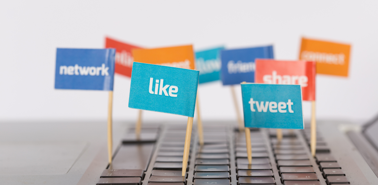 Colorful mini flags with social media words like “like”, “tweet”, and “share” on a laptop keyboard