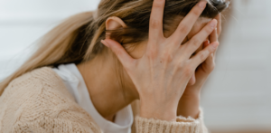 Distressed woman with hands covering her face, wearing a beige sweater, showing emotional stress