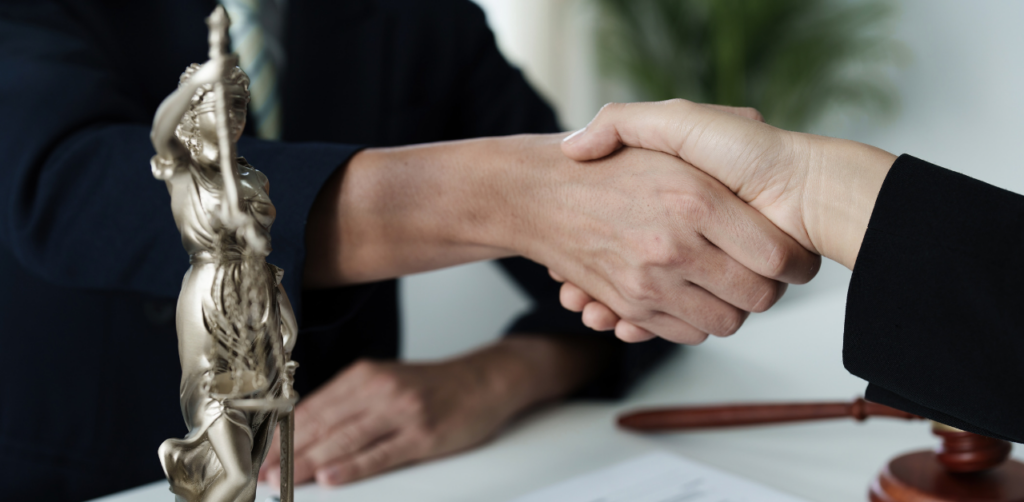 Handshake between two professionals with Lady Justice statue and gavel, symbolizing legal services agreement