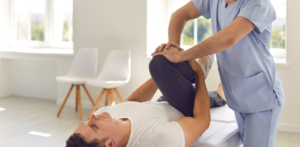 Physiotherapist assisting patient with leg stretches during rehabilitation session in a bright clinic room