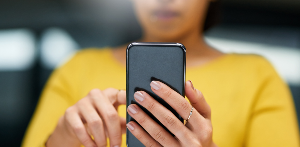 Woman in yellow shirt using smartphone, focusing on screen and typing with manicured fingers