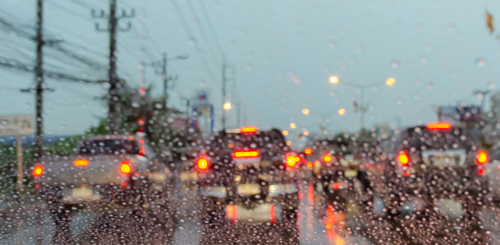 Blurred view of cars stuck in traffic on a rainy day, seen through a windshield with water droplets