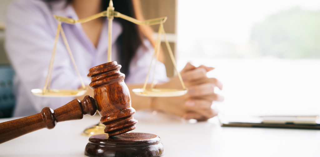 Gavel and justice scales on desk with woman in background, symbolizing legal proceedings or court cases