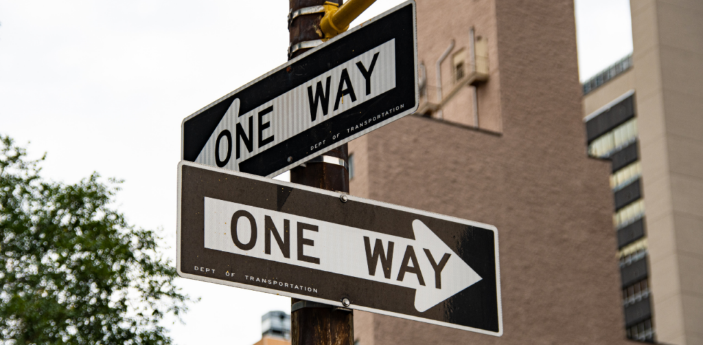 Two conflicting “One Way” street signs pointing in opposite directions on a pole in an urban setting