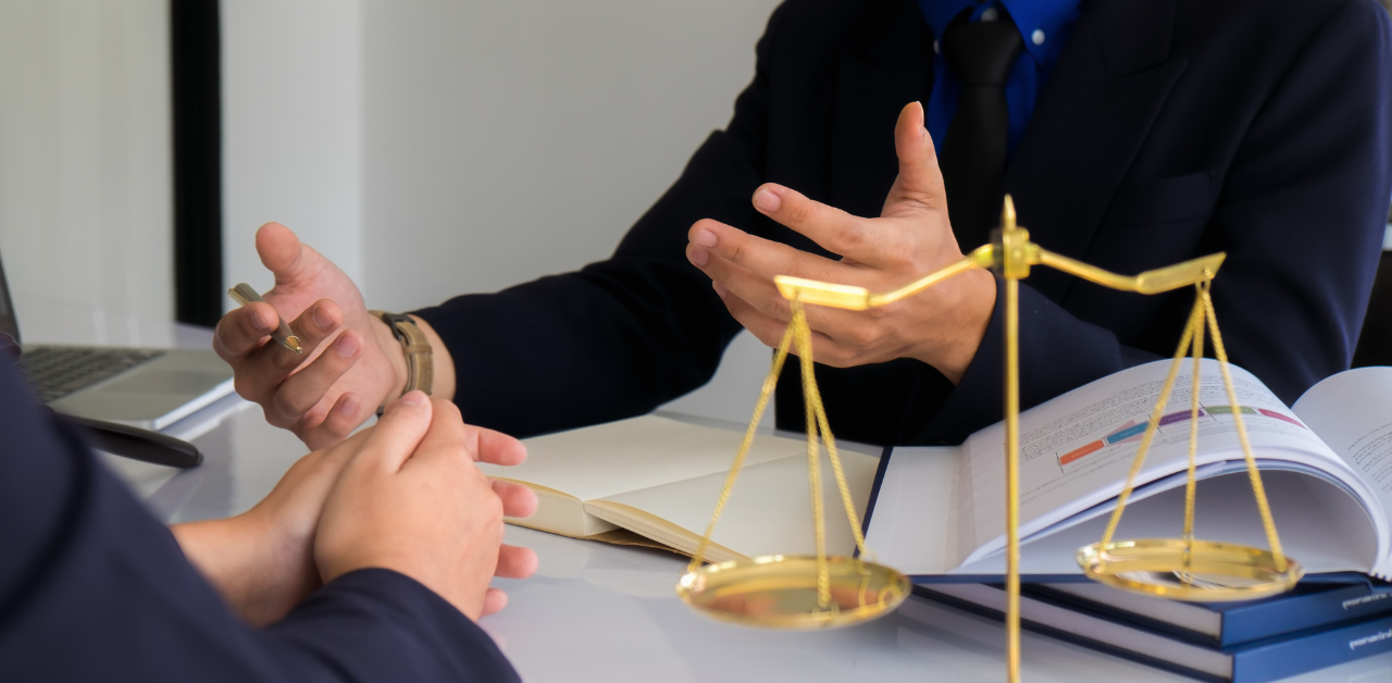 Two people in discussion at a desk with open books and golden scales, symbolizing legal advice or counsel