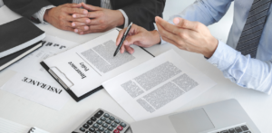 Close-up of businesspeople reviewing a car insurance policy at a desk with documents, pens, and a calculator