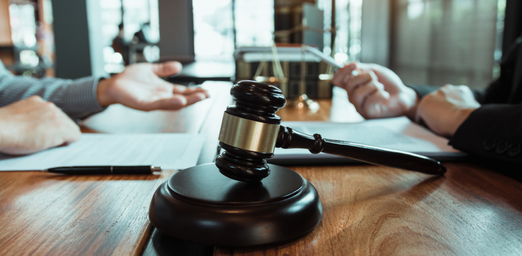 Close-up of gavel on table with two people discussing legal documents in background