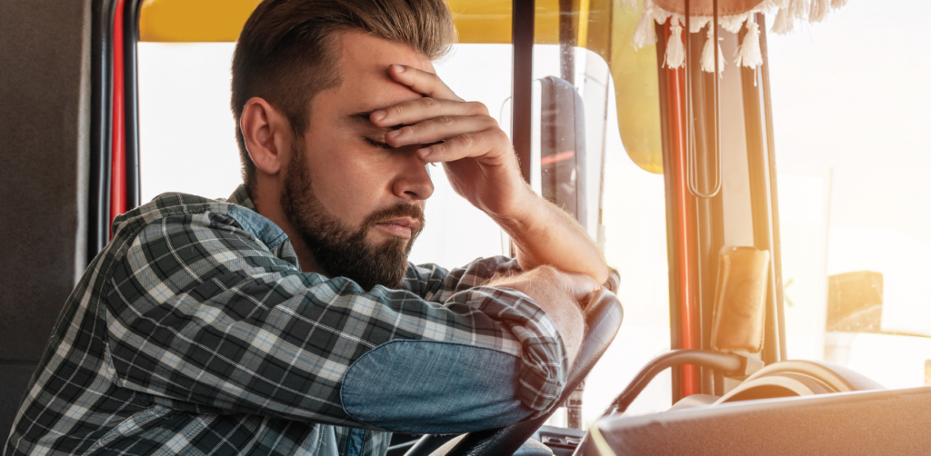 Exhausted truck driver in a plaid shirt resting his head on the steering wheel, eyes closed from fatigue