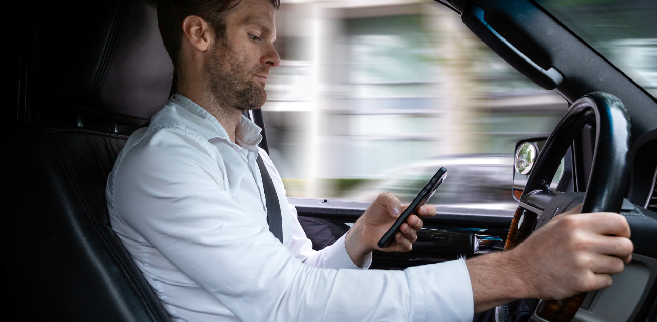 Man in white shirt texting while driving, distracted behind the wheel of a moving vehicle