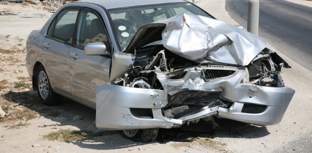 Silver car with severe front-end damage from a collision parked on roadside after crash