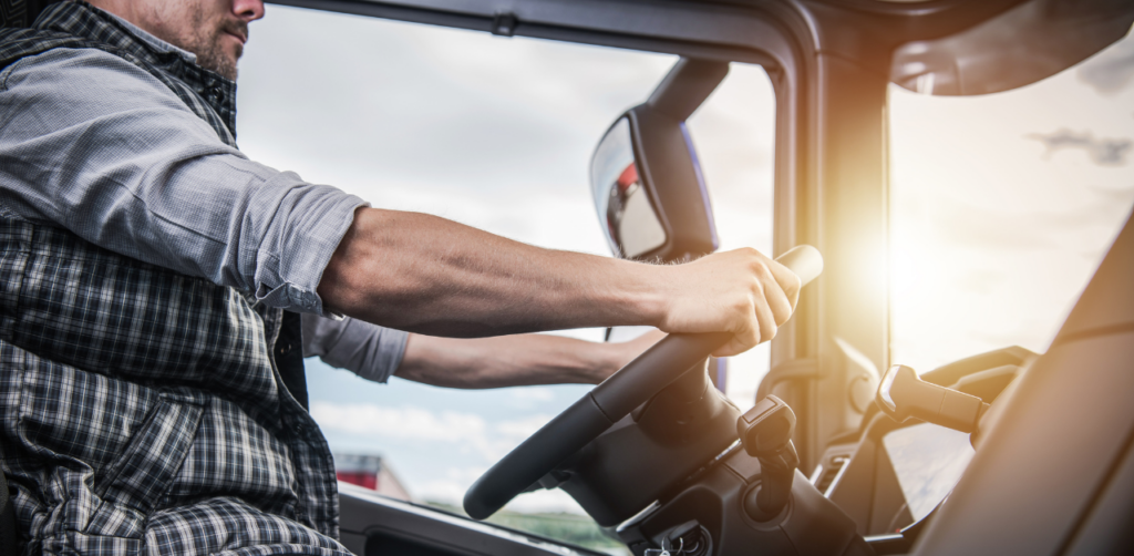 Truck driver gripping steering wheel while driving a large vehicle during daylight