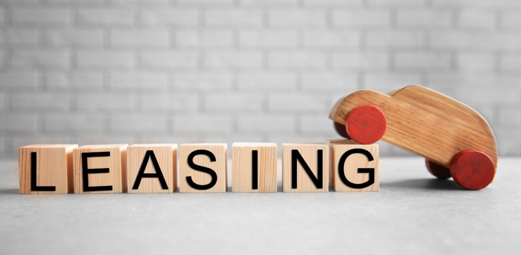 Wooden toy car leaning on blocks spelling “LEASING,” symbolizing car leasing concept