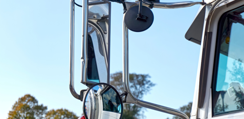 Close-up of a truck mirror setup with a mounted vehicle camera system against a clear blue sky