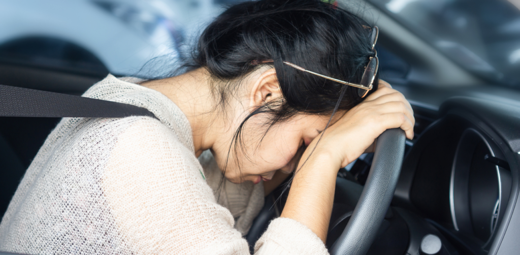 Stressed woman resting her head on a steering wheel inside a car, showing emotional distress