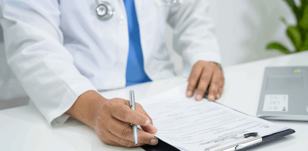 A doctor fills out a medical form on a clipboard at a white desk with a laptop nearby