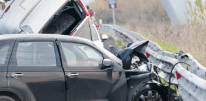 A severe multi-vehicle crash shows a black car crushed into a guardrail and a van stacked on top