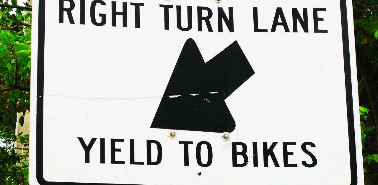Damaged street sign reading Right Turn Lane Yield to Bikes with a partially obscured graphic in black and white