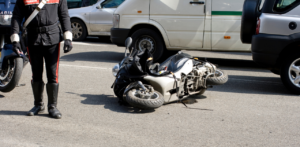 Fallen scooter on the road beside a police officer and parked vehicles