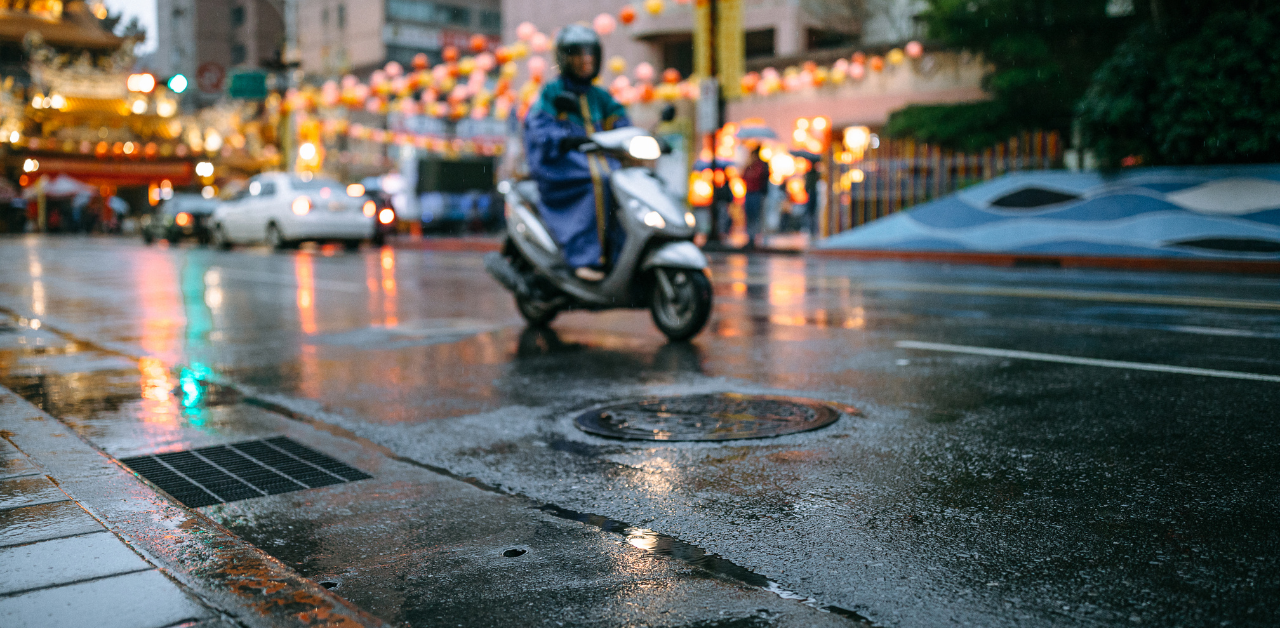Person riding a scooter through wet city streets on a rainy evening