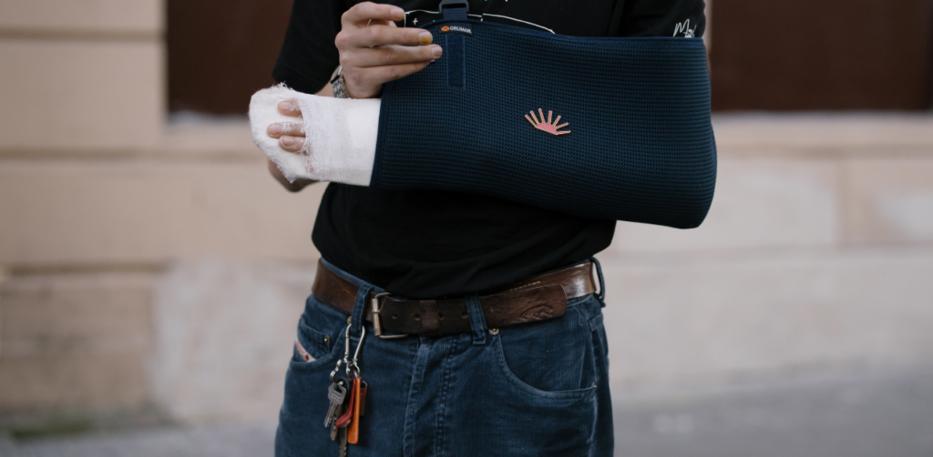Person wearing a black shirt and blue jeans with a broken arm in a navy blue sling and white bandage wrap