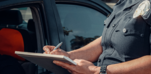 Police officer writing a ticket on a notepad beside a parked car during a traffic stop