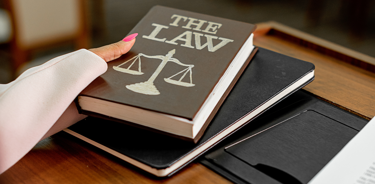 Close-up of a hand with pink nails resting on a hardcover book titled “The Law,” featuring a scales of justice symbol, representing legal authority and legal rights