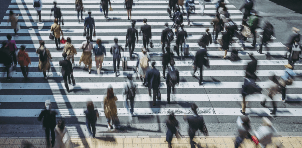Large crowd of people moves across a wide crosswalk in a busy urban intersection, emphasizing the importance of pedestrian right-of-way and traffic safety