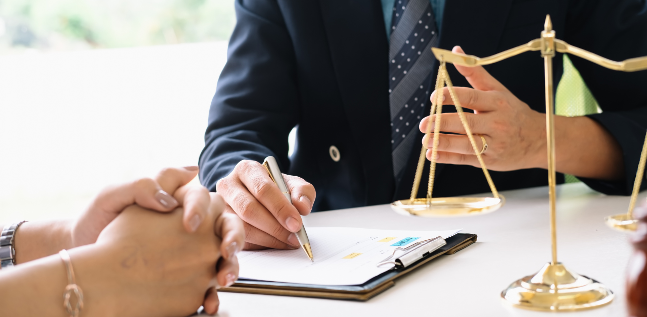 Lawyer in a dark suit explains legal options to clients across a desk, with a justice scale and notepad in view, symbolizing legal support after an auto accident