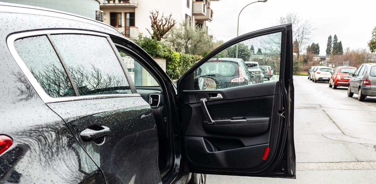 Car door left wide open on street with parked cars, increasing dooring accident risk