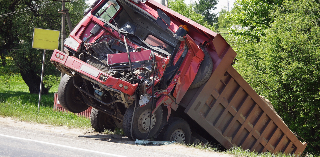 Crashed red dump truck with severe front-end damage tilted off-road near trees and power lines