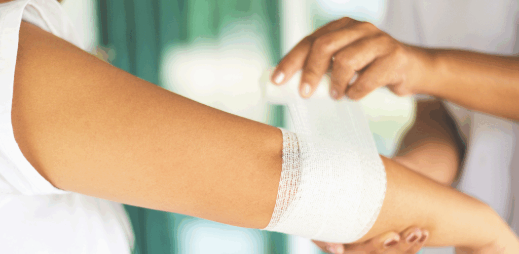 Person wrapping a white bandage around an injured arm in a medical or first aid setting
