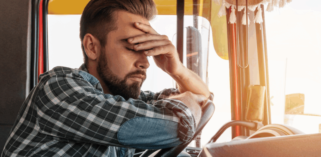 Male truck driver in plaid shirt looks exhausted, suggesting fatigue before truck accident investigation