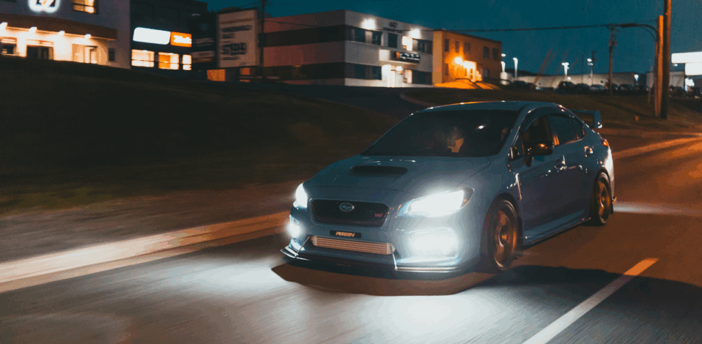Blue sports car drives fast at night with headlights on a city street