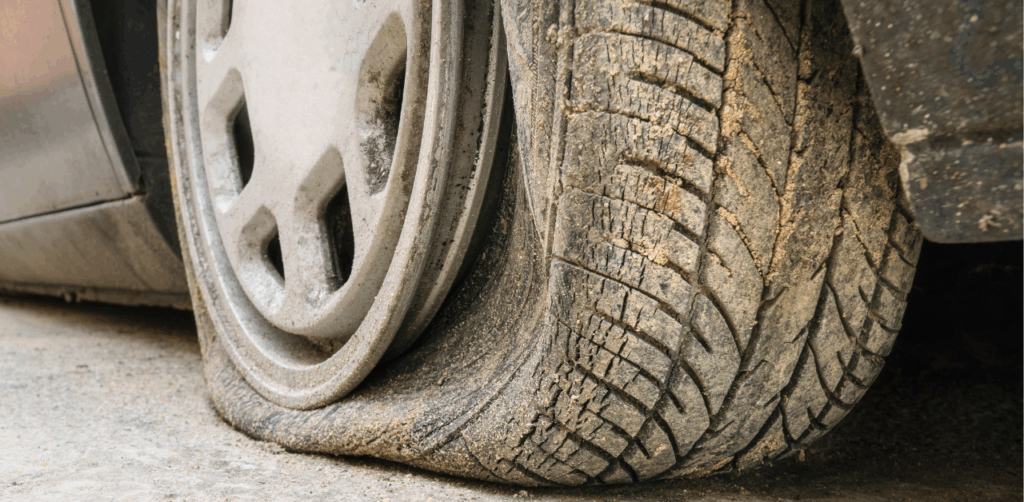 Close-up of a flat car tire with worn tread and dirt buildup on a city street