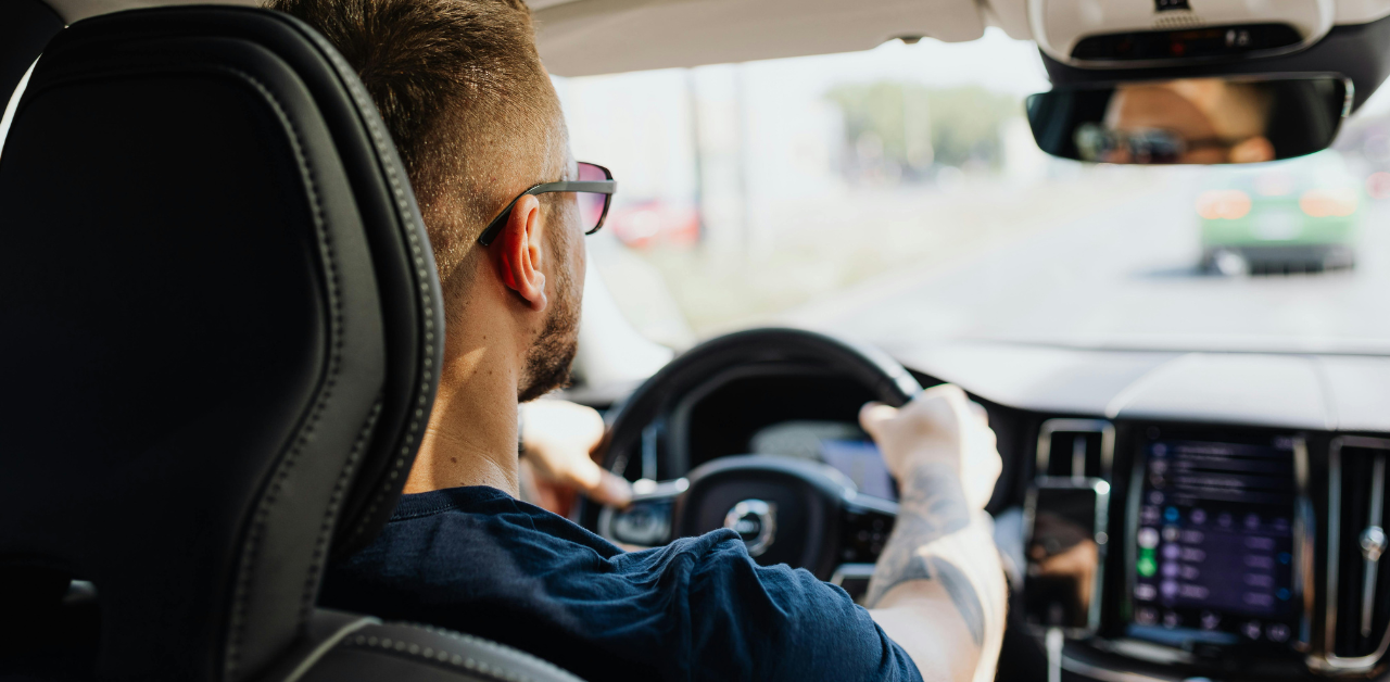 Man driving a car, hands on the wheel, viewed from the back seat