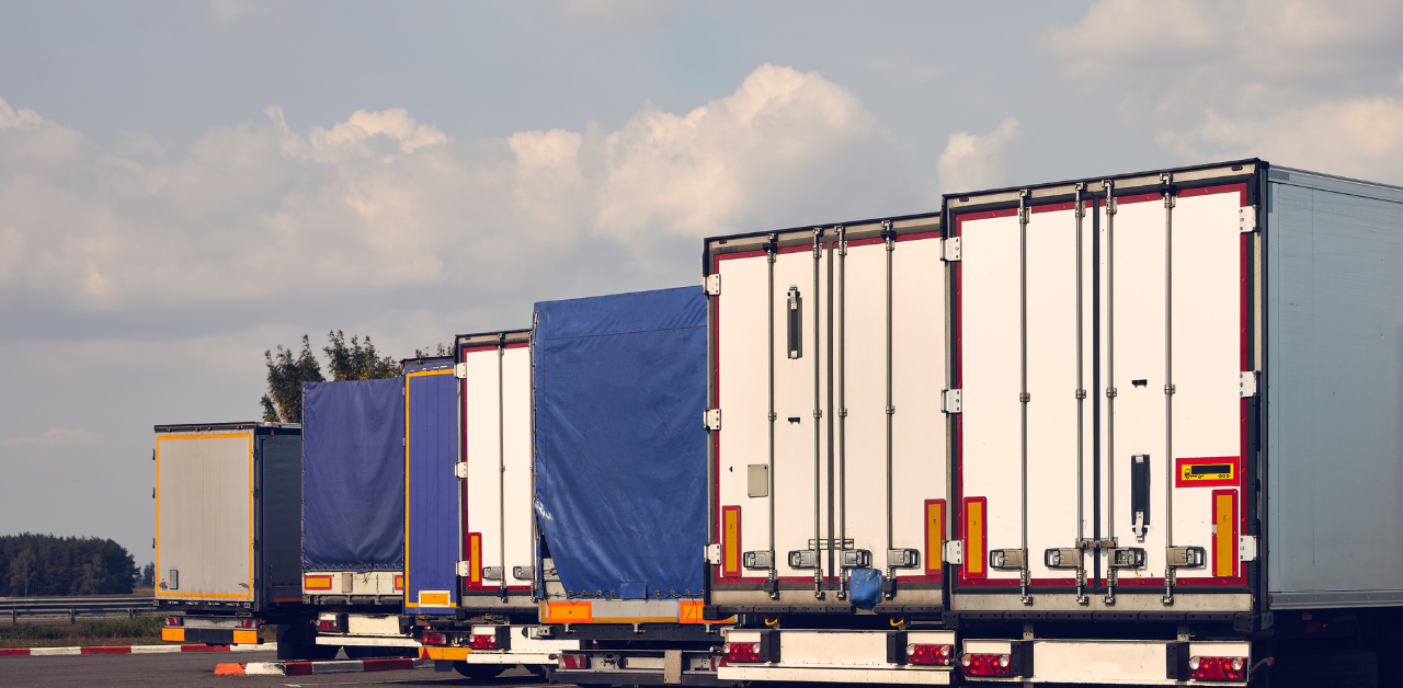 Parked freight trucks lined up at a rest area under a partly cloudy sky