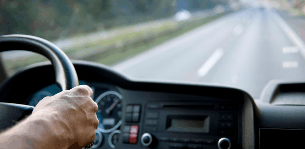 Truck driver’s hand on the wheel while driving down a highway
