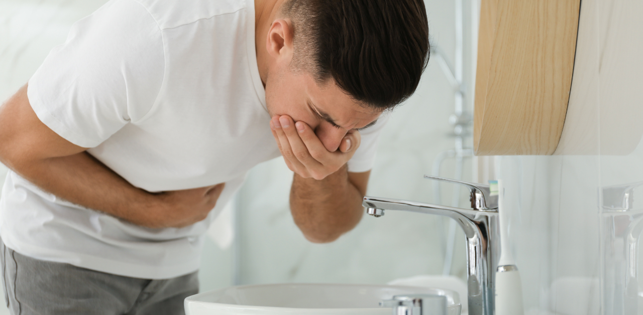 Man leaning over sink holding stomach and mouth, showing nausea, stomach pain, or illness symptoms at home