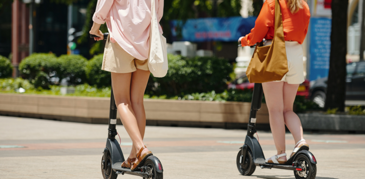 Two women riding electric scooters on a city street, highlighting urban micromobility and transportation safety